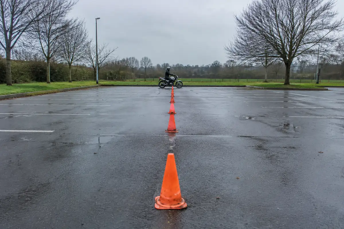 Moto à l'arrêt au bout d'une file de plots sur un parking servant de plateau d'exercice